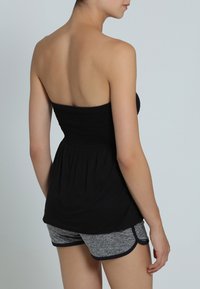 Zwarte strapless top met een gerimpelde-borst en een vloeiende onderkant, gecombineerd met grijze sportshorts met een contrasterende tailleband en bies.