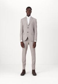 Fato cinza claro, ajustado, com lapela notched, dois botões e bolsos laterais. Camisa branca por baixo, complementada por sapatos castanho-escuros.