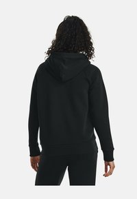 Felpa nera con cappuccio, dal taglio rilassato, con polsini e orlo a costine e una texture morbida. Presenta una tasca a marsupio e un design minimalista.