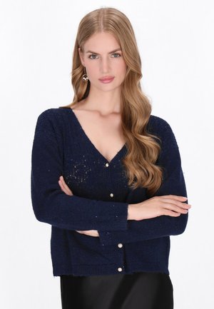 Navy blauwe cardigan met een V-hals, lange mouwen en parelknoopjes. Gemaakt van een textuurgebreide stof met een iets cropped pasvorm.
