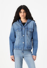 Τζάκετ από τζην σε ανοιχτό μπλε χρώμα με κουκούλα, δύο τσέπες στο στήθος και κλείσιμο με κουμπιά. Διαθέτει χαλαρή εφαρμογή και εμφανείς λεπτομέρειες στο ραφές.