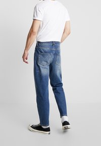Light-wash blue denim jeans with a straight leg, featuring a faded effect, back pockets, and a high-rise waistband. Worn with black sneakers.