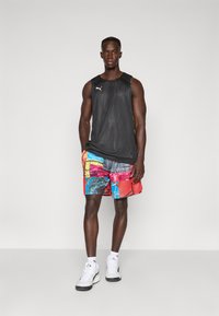 Sort ærmeløs sports T-shirt, farverige grafiske shorts med geometriske mønstre, hvide sportsko, stående på en ensfarvet baggrund.