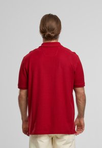 Röd kortärmad polo med klassisk krage och rak passform. Har en subtil textur och sömdetaljer på baksidan.