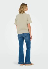 Lyse beige struktureret kortærmet top parret med blå klokkeformede jeans. Outfittet har en afslappet pasform og synlige syninger på jeansene.
