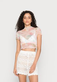 Top transparente e cropped com padrão mármore em tons pastéis, mangas curtas e bordas serrilhadas, combinado com calções brancos em malha aberta com cordão.