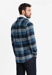 Camisa de franela a cuadros en tonos marino y gris con puños abotonados y cuello. Presenta un lazo colgante en la parte posterior y una textura suave.