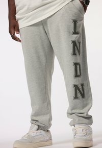 Grijze joggingbroek met een relaxte pasvorm, voorzien van de tekst "LNDN" in donkergroen aan de zijkant. Gemaakt van zachte stof met elastische boorden en tailleband.
