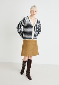 Navy and white striped knit cardigan with a v-neck, cream buttons, paired with a brown corduroy skirt and knee-high brown leather boots.