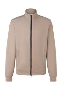 Beige zip-jakke med ståkrave, lange ærmer, to forlommer og en sort lynlås, der løber ned langs midten fortil.