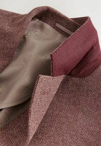 Veste en mélange de laine dans un bordeaux foncé, avec un tissu extérieur texturé. Intérieur doublé d'un tissu léger à motifs. Détail de col cranté visible.