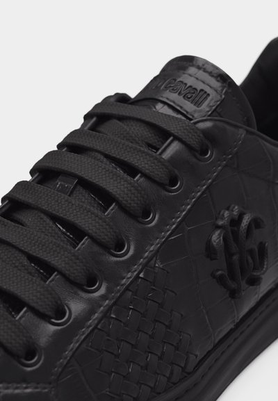 Gros plan sur une basket en cuir noir avec un détail tissé sur le côté, des lacets noirs et un logo embossé sur le panneau latéral.