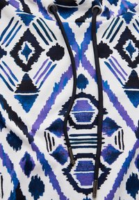 Hoodie in het wit met een geometrisch patroon in blauw, paars en zwart. Bevat zwarte trekkoorden en metalen aglets.