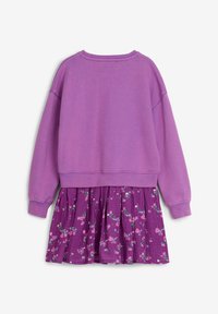 Lila Sweatshirt mit langen Ärmeln, kombiniert mit einem lila Rock mit floralem Muster aus strukturiertem Stoff, der einfarbige und bedruckte Elemente vereint.