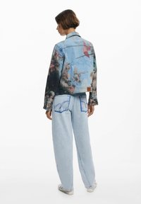 Veste en denim avec un imprimé artistique coloré, accompagnée de jeans à jambes larges délavés et de baskets blanches. Manches longues et col.