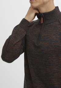 Maglione lavorato a maglia con colletto alto, dotato di mezzo zip. Base blu navy scuro con un motivo melangiato arancione, polsini e collo a coste.