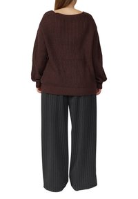 Bordowy sweter z dzianiny o luźnym fasonie i opuszczonych ramionach, zestawiony z szerokimi czarnymi spodniami w prążki. Teksturowany, luźny design.