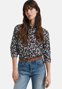 Blusa nera a fiori con maniche lunghe, chiusura a bottoni e colletto; abbinata a jeans in denim azzurro chiaro e una cintura in pelle marrone.