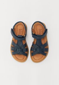 Mørkeblå lær sandaler med kryssremmer og en sløyfedetalj; lys brun innersåle og gummisåle; justerbar ankelreim med gullfeste.