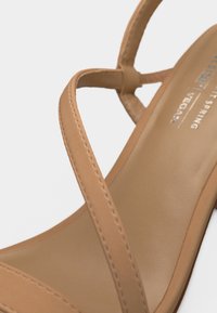 Κοντινό πλάνο μπεζ δερμάτινου σανδαλιού με λεπτούς ιμάντες και λείο πέλμα, δείχνοντας ελάχιστες ραφές.