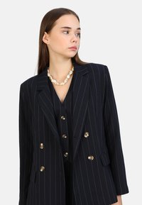 Blazer marine à rayures fines avec un design à double boutonnage, boutons dorés et coupe ajustée, présentant un col cranté et une texture de tissu lisse.