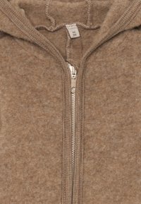 Hnědá fleecová mikina na zip s texturovanou látkou. Obsahuje kovový zip a kapuci na šňůrku. Štítek ukazuje velikost 56 a pokyny k údržbě.