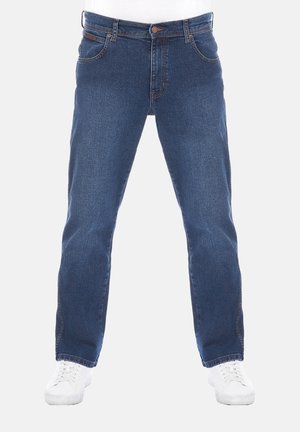 Blaue Jeans mit geradem Schnitt, getragen mit weißen Turnschuhen, von der Taille bis zu den Füßen auf weißem Hintergrund gezeigt.