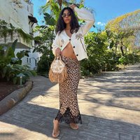 Weißer Cardigan mit Blumenstickerei, Maxi-Rock mit Leopardenmuster und Spitzenbesatz, beige Handtasche mit Fransen, Sandalen, tropischer Hintergrund.