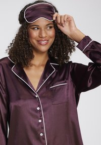Purple satin pajama set with white piping, featuring a button-up shirt and a pocket. Includes a matching satin sleep mask.