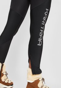 Svarta sportleggings har en siddragkedja och grå logo-text. Slät tyg med kontrasterande paneldesign. Fodrade bruna stövlar av sherling nedan.