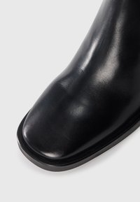 Czarne skórzane buty z gładką, błyszczącą powierzchnią, zaokrąglonym noskiem i minimalistycznym designem z delikatnym bieżnikiem na podeszwie.