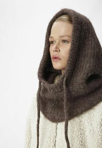 Écharpe à capuche en tricot marron avec une texture douce, présentant un grand design de col et des cordons de serrage, associée à un manteau texturé crème.
