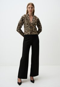 Maglione a stampa leopardata con scollo a V e dettagli con frange, abbinato a pantaloni neri a vita alta e décolleté neri a punta.