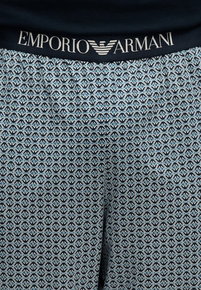 Sous-vêtements avec une ceinture foncée comportant le texte et le logo "EMPORIO ARMANI", ainsi qu'un motif géométrique répétitif sur le tissu en dessous.