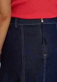 Tumši zila džinsu svārki ar kontrastējošām baltām šuvēm, aizmugurējais rāvējslēdzis un neliels elastīgs detalizējums viduklī.