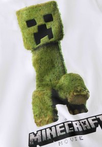 Vihreä kömpelö hahmo, jolla on pikselöity kasvot, esitetty valkoisessa paidassa tekstin "A MINECRAFT MOVIE" alla. Teksti on paksua ja tyyliteltyä.