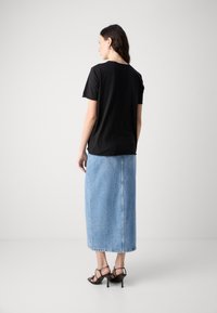T-shirt nero a maniche corte abbinato a una maxi gonna in denim azzurro. L'outfit è completato da sandali con cinturini neri.