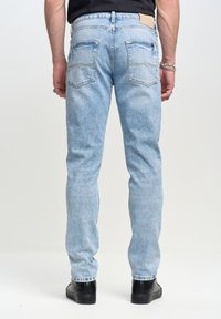 Jeans de mezclilla azul claro con corte recto, cinco bolsillos y parche de cuero en la cintura. Cuenta con costuras sutiles y un acabado desgastado.
