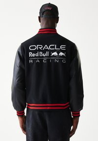 Μαύρο μάλλινο και δερμάτινο varsity μπουφάν με ριγέ κόκκινη πλεκτή λωρίδα. Διαθέτει μεγάλα τυπωμένα λογότυπα: "ORACLE Red Bull RACING" στην πλάτη.