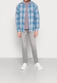 Niebiesko-biała flanelowa koszula w kratę na jasnofioletowej koszulce, do tego jasnoszare dżinsy i białe trampki.