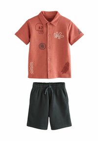 Kurzes oranges Shirt mit gestickten Designs, kombiniert mit dunkelgrünen Shorts mit elastischem Bund.