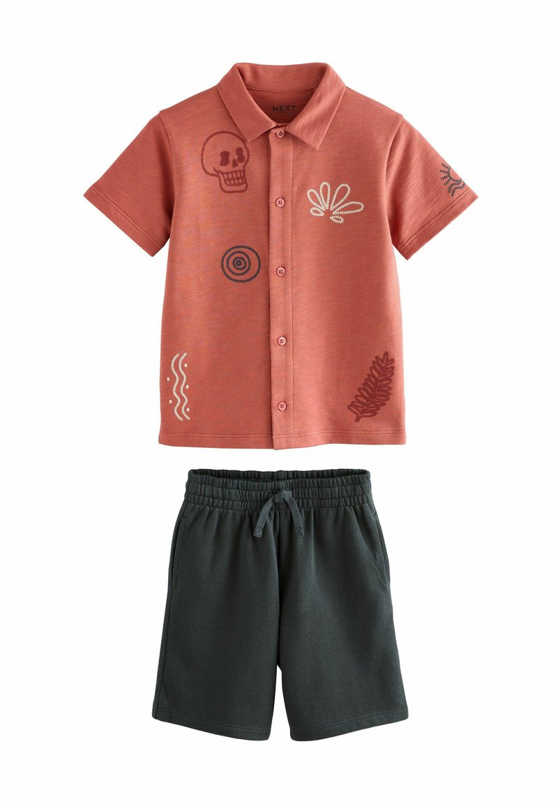 Kurzes oranges Shirt mit gestickten Designs, kombiniert mit dunkelgrünen Shorts mit elastischem Bund.