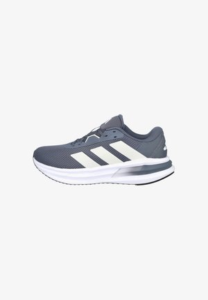 Zapatilla deportiva gris con una parte superior de malla y detalles de rayas blancas. Presenta una suela acolchada y un diseño de punta redondeada para mayor comodidad.