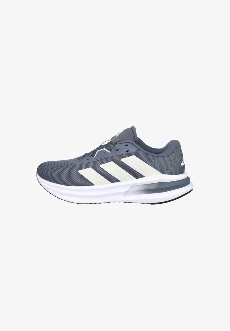 Zapatilla deportiva gris con una parte superior de malla y detalles de rayas blancas. Presenta una suela acolchada y un diseño de punta redondeada para mayor comodidad.