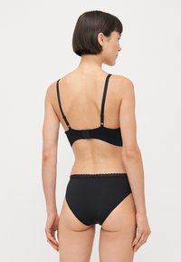 Zwarte bh en bijpassende set met slips, beide gemaakt van gladde stof. De bh heeft verstelbare banden en een haaksluiting. De slip heeft een golvende tailleband.