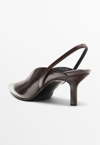 Scarpa slingback in pelle marrone con punta affusolata, finitura testurizzata e tacco sottile. Il cinturino è liscio e si integra con il design elegante della scarpa.