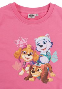 T-shirt rosa in cotone con tre cani dei cartoni animati di colori distinti: marrone chiaro, bianco e marrone scuro, su uno sfondo vivace.