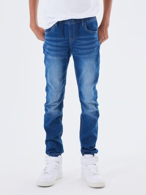 Jeans in denim blu sbiadito con taglio dritto, cinque tasche e dettagli di cucitura. Abbinati a sneaker alte bianche.