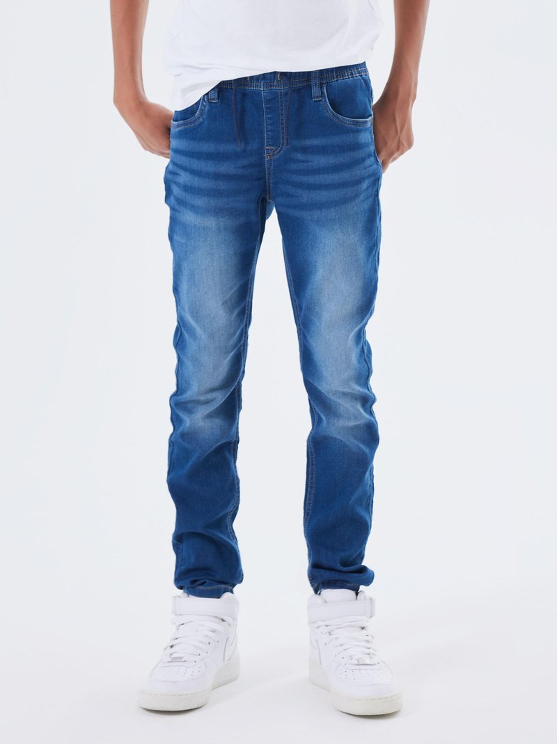 Jeans in denim blu sbiadito con taglio dritto, cinque tasche e dettagli di cucitura. Abbinati a sneaker alte bianche.
