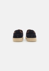 Navy suede shoes with tan leather accents, rubber sole, and decorative stitching at the heel, shown from the back.